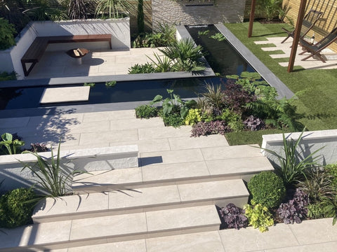 An overhead view of a garden featuring a pathway and seating area laid out with beige porcelain paving stones.