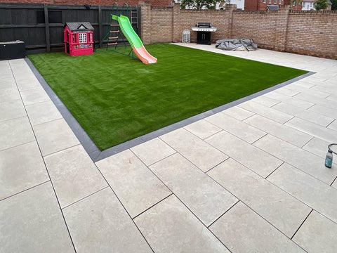 A beige porcelain tile with a solid color and flickers of white, laid out on the ground in a garden setting with a slide and a red house in the background.