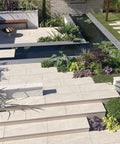 An overhead view of a garden featuring a pathway and seating area laid out with beige porcelain paving stones.